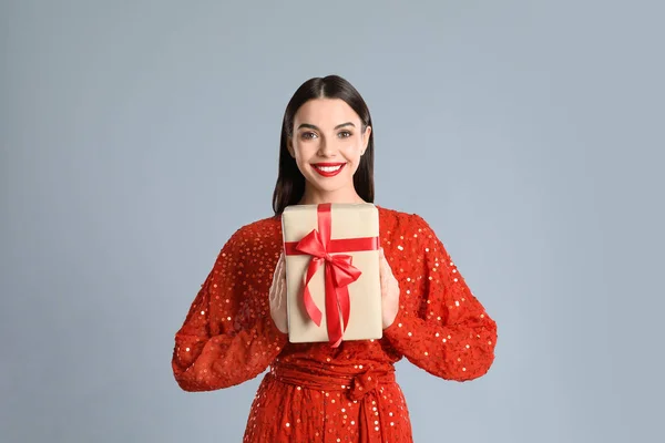 Žena Červených Šatech Drží Vánoční Dárek Šedém Pozadí — Stock fotografie