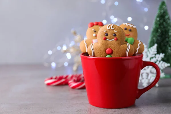 Gingerbread men in cup on light table against blurred lights, space for text