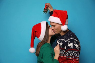 Mutlu çift ökseotunun altında öpüşüyor açık mavi arka planda