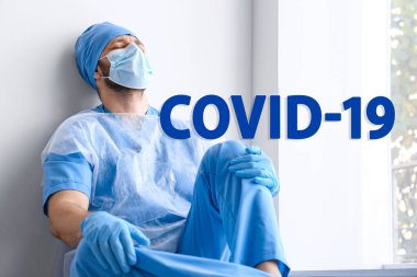 Hastanede duvarın yanında oturan yorgun doktor. Coronavirüs salgını sırasında tıbbi sistem çökmüş.