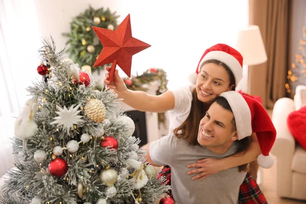 室内にクリスマスツリーを飾るカップル 星のトッパーに焦点を当てる — ストック写真