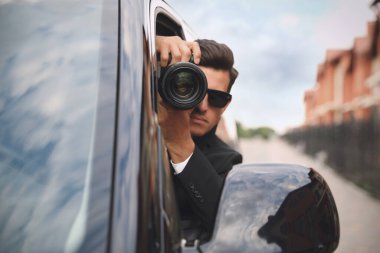 Kameralı özel dedektif arabadan gözetliyor.