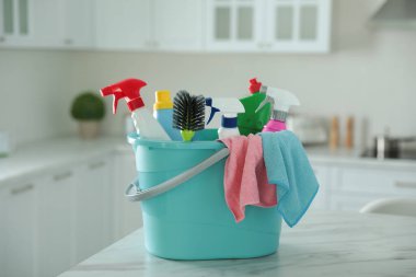 Mutfaktaki masada farklı temizlik malzemeleriyle plastik kova.