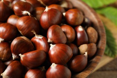 Fresh sweet edible chestnuts in wooden bowl, closeup clipart