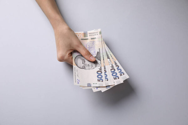 Woman holding Ukrainian money on light grey background, closeup