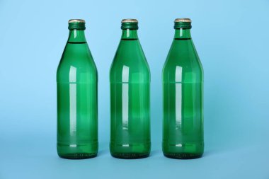 Glass bottles with water on light blue background