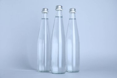 Beyaz zemin üzerinde su olan cam şişeler.
