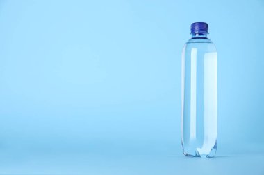 Plastic bottle with water on light blue background, space for text