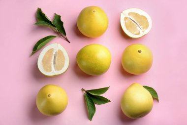 Fresh cut and whole pomelo fruits with leaves on pink background, flat lay