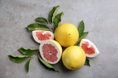 Fresh cut and whole pomelo fruits with leaves on light grey table, flat lay