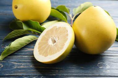 Fresh cut and whole pomelo fruits on blue wooden table, closeup