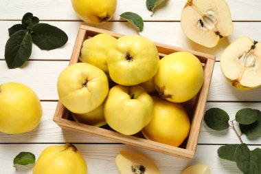 Fresh ripe organic quinces and leaves on white wooden table, flat lay