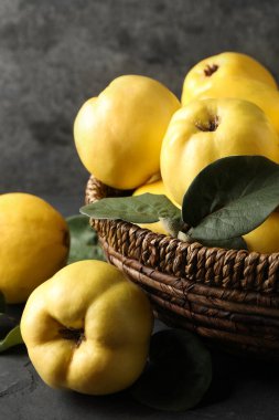 Fresh ripe organic quinces with leaves in wicker basket on table, closeup
