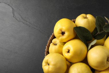 Fresh ripe organic quinces with leaves in wicker basket on black table, closeup. Space for text