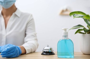 Otelin tezgahındaki resepsiyonist, antiseptik jel ve servis zili olan şeker şişesine odaklan.