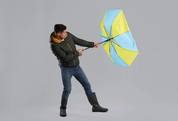 灰色の背景に風の突風に巻き込まれた傘を持つ男 — ストック写真