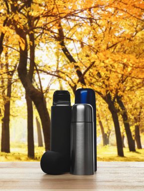 Sonbahar parkında ahşap masada farklı termoslar.