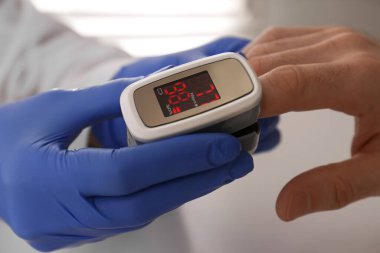 Doktor hastanın oksijen seviyesini nabız oksimetresiyle kontrol ediyor açık gri masada, yakın plan.