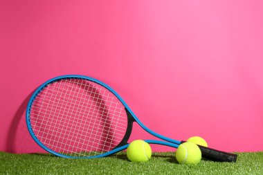 Tenis raketi ve toplar yeşil çimlerin üzerinde pembe arka plana karşı. Metin için boşluk