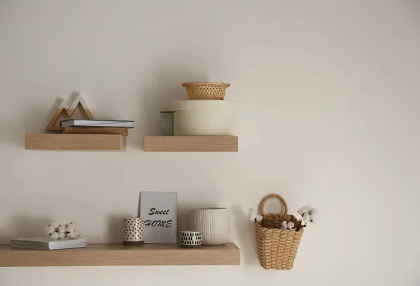 Wooden shelves with books and different decorative elements on light wall. Space for text