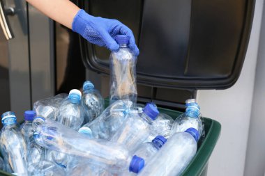 Eldivenli kadın, kullanılmış plastik şişeyi dışarıdaki çöp kutusuna koyuyor, yakın plan. Geri dönüşüm sorunu