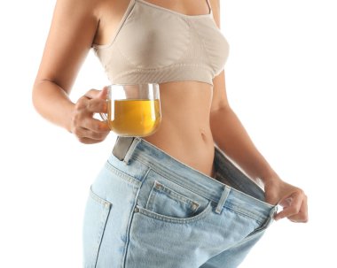 Yaşlı, büyük kotlu ve elinde çay bardağı olan genç bir kadın beyaz arka planda diyet sonuçlarını gösteriyor.