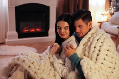 Kareli elbiseli çift şöminenin yanında oturuyor.