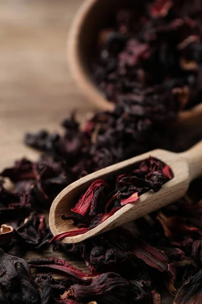 Wooden scoop with dry hibiscus tea on table, closeup