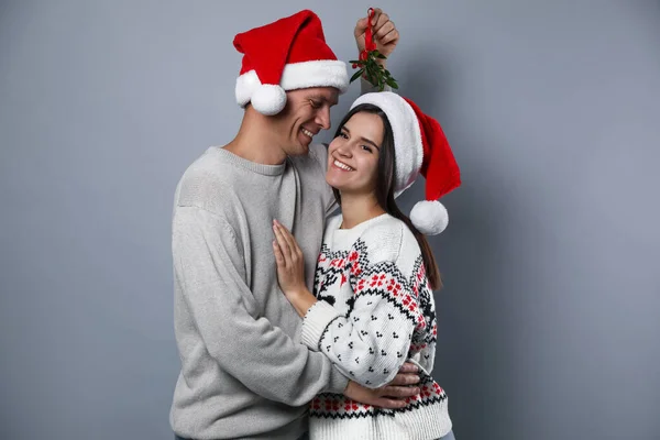 戴着圣诞礼帽的一对快乐的夫妇站在一群灰蒙蒙的寄生下 — 图库照片