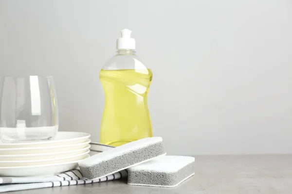 Cleaning product and sponges near plates on grey table, space for text. Dish washing supplies