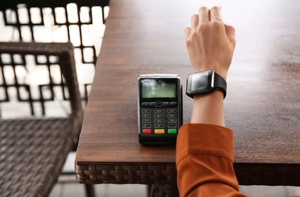 Woman making payment with smart watch at table, closeup