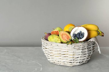 Gri masadaki sepette taze egzotik meyveler var.