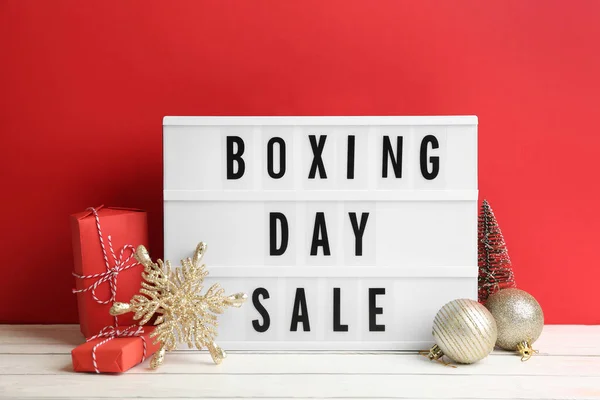 Composition with Boxing Day Sale sign and Christmas gifts on white table against red background