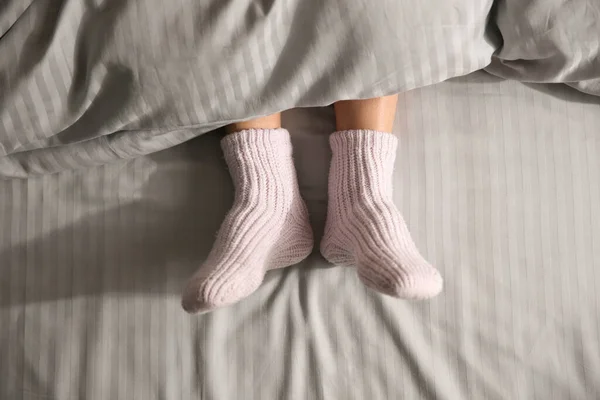 Woman wearing knitted socks under blanket in bed, top view