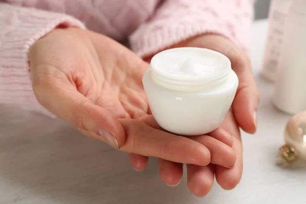 Woman holding jar of cream at light table, closeup. Cosmetic product for winter