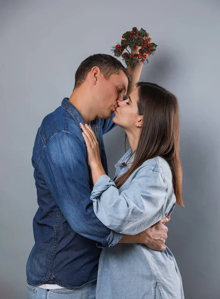 Happy Couple Kissing Mistletoe Wreath Grey Background — Stock Photo, Image