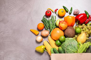 Gri masadaki taze organik meyve ve sebzelerle dolu kağıt torba. Metin için boşluk