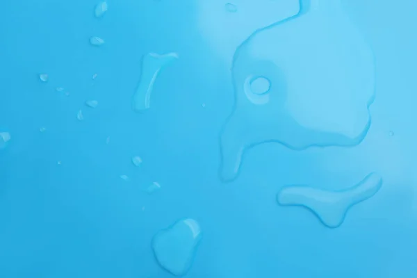 光の青の背景にこぼれた水の滴 トップビュー — ストック写真