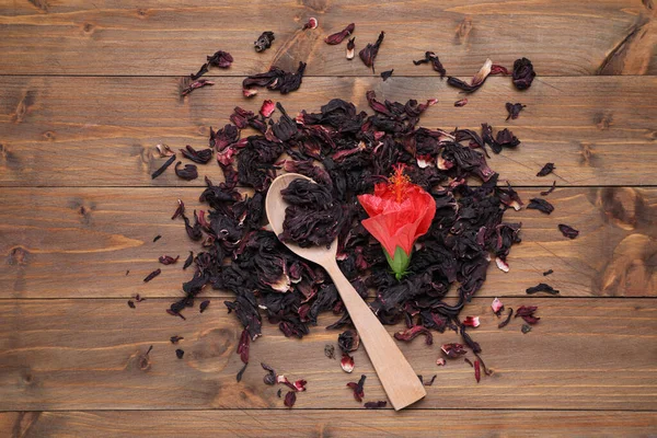 Dry hibiscus tea, spoon and flower on wooden table, flat lay