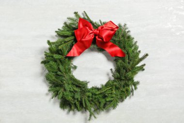 Beyaz arka planda kırmızı kurdeleli köknar dallarından yapılmış Noel çelengi