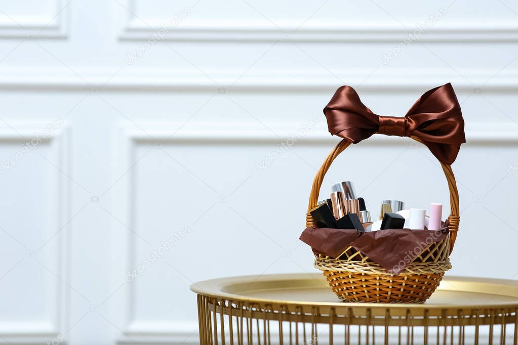 Gift set in wicker basket on golden table near white wall. Space for text