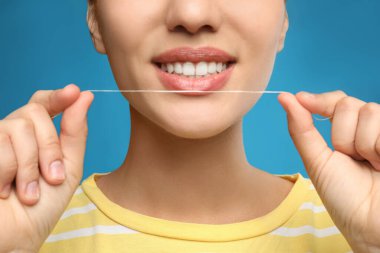Dişlerini mavi arka planda diş ipi ile temizleyen genç bir kadın, yakın plan. Kozmetik dişçiliği