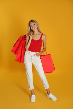 Sarı arka planda alışveriş torbaları olan mutlu genç bir kadın. Kara Cuma İndirimi