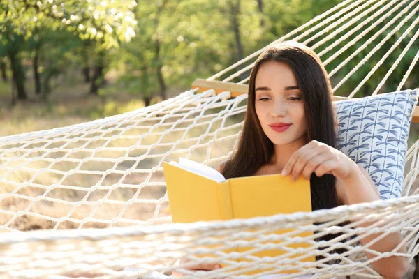 在绿色花园舒适的吊床上看书的年轻女人 — 图库照片