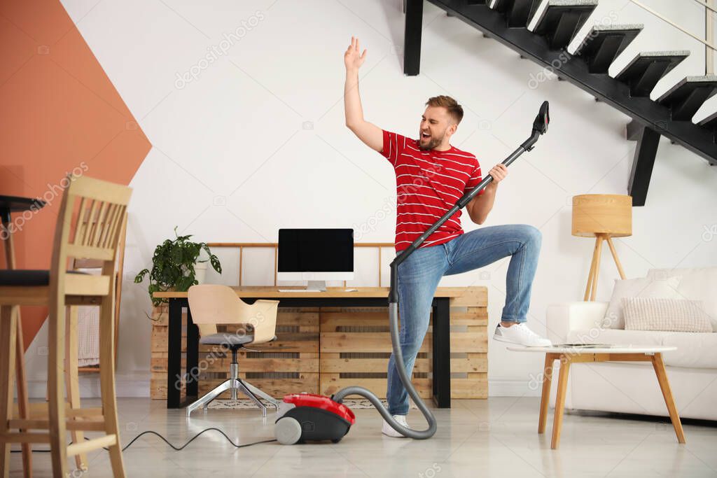 Young man having fun while vacuuming at home