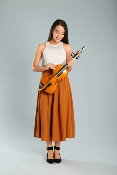 Beautiful woman with violin on grey background