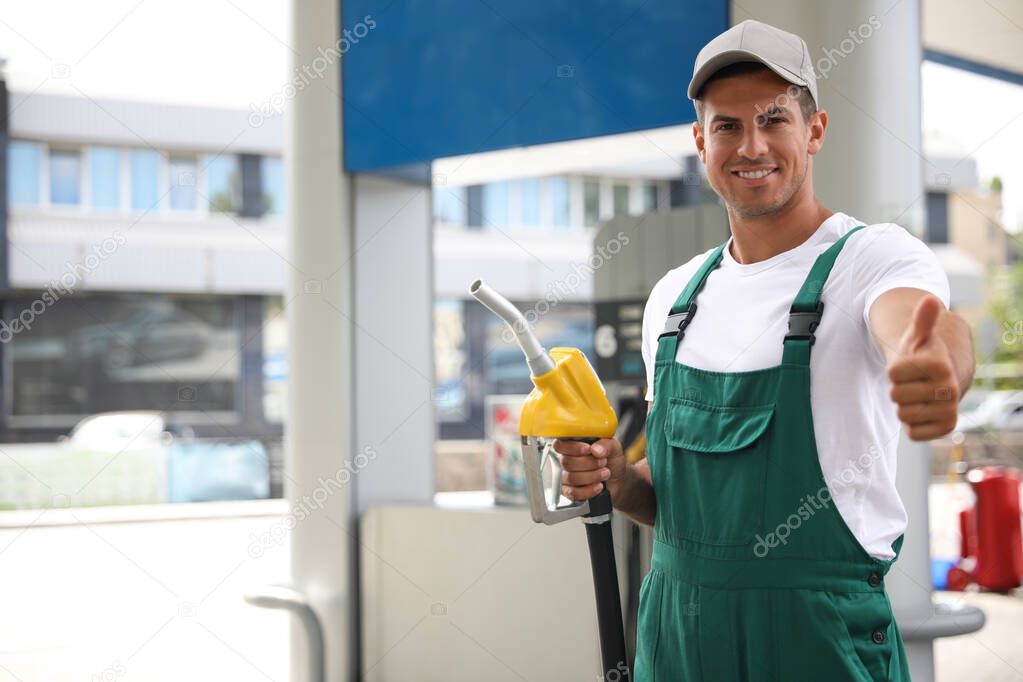 Worker with fuel pump nozzle at modern gas station