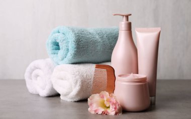 Farklı saç ürünleri, rulo havlular ve gri masada ahşap tarak.