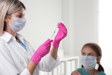 Hastanede küçük bir kız için şırıngayı aşıyla dolduran doktor.