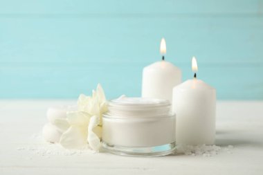 Kremalı spa kompozisyonu, mumlar ve çiçekler beyaz masada.